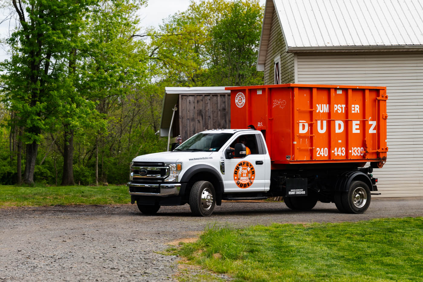 A truck brings the perfect sized Dumpster Dudez dumpster to a home for a cleanup project - contact us today to learn more about our dumpster sizes!
