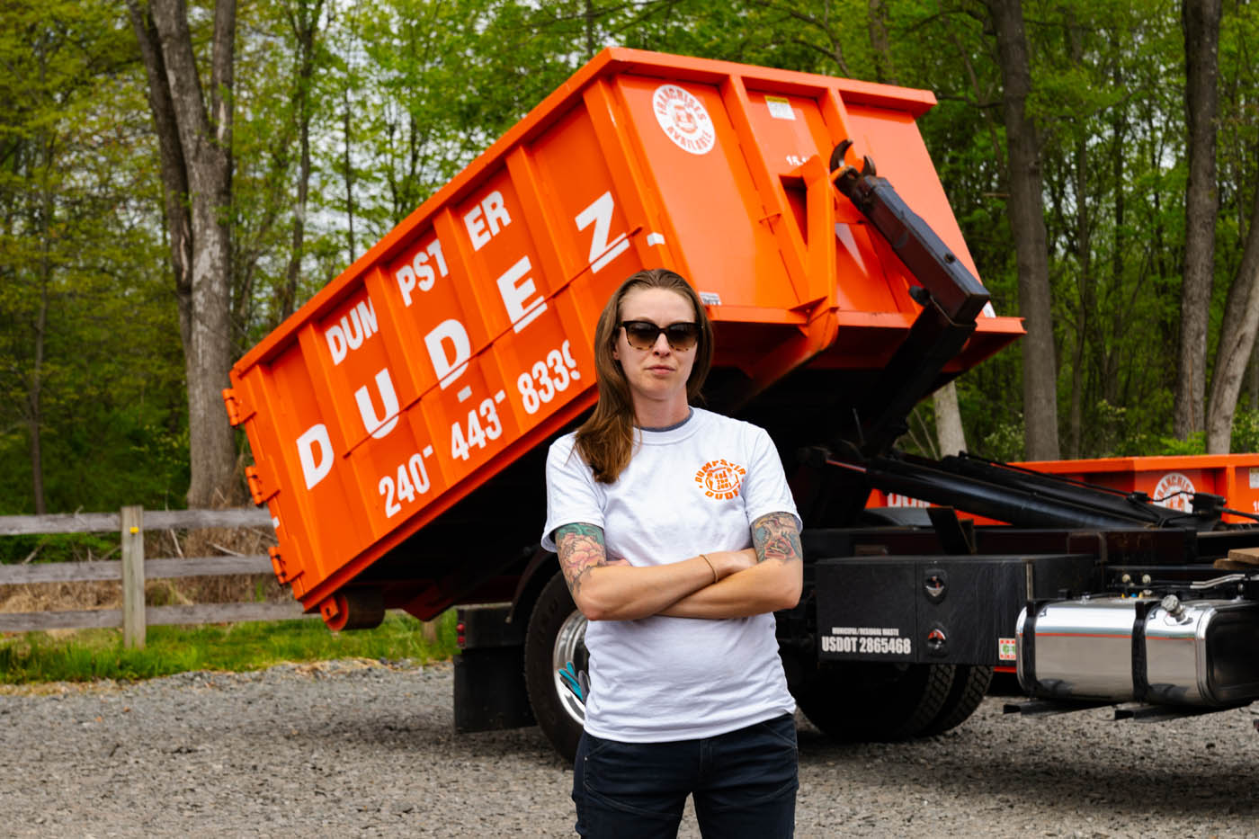 A Dumpster Dudez employee standing in front of an orange dumpster truck.