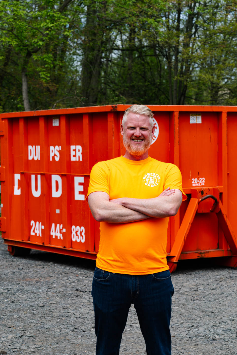 
				A Dumpster Dudez employee standing in front of a large dumpster ready to rent.
			