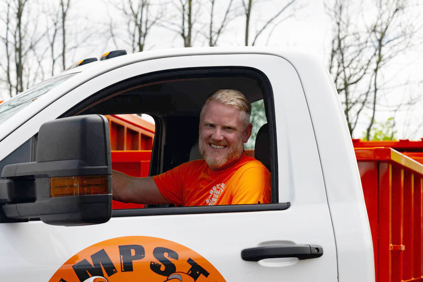 A Dumpster Dudez team member sitting in a company dumpster, contact Dumpster Dudez for more information on household hazardous waste disposal in Omaha, NE.