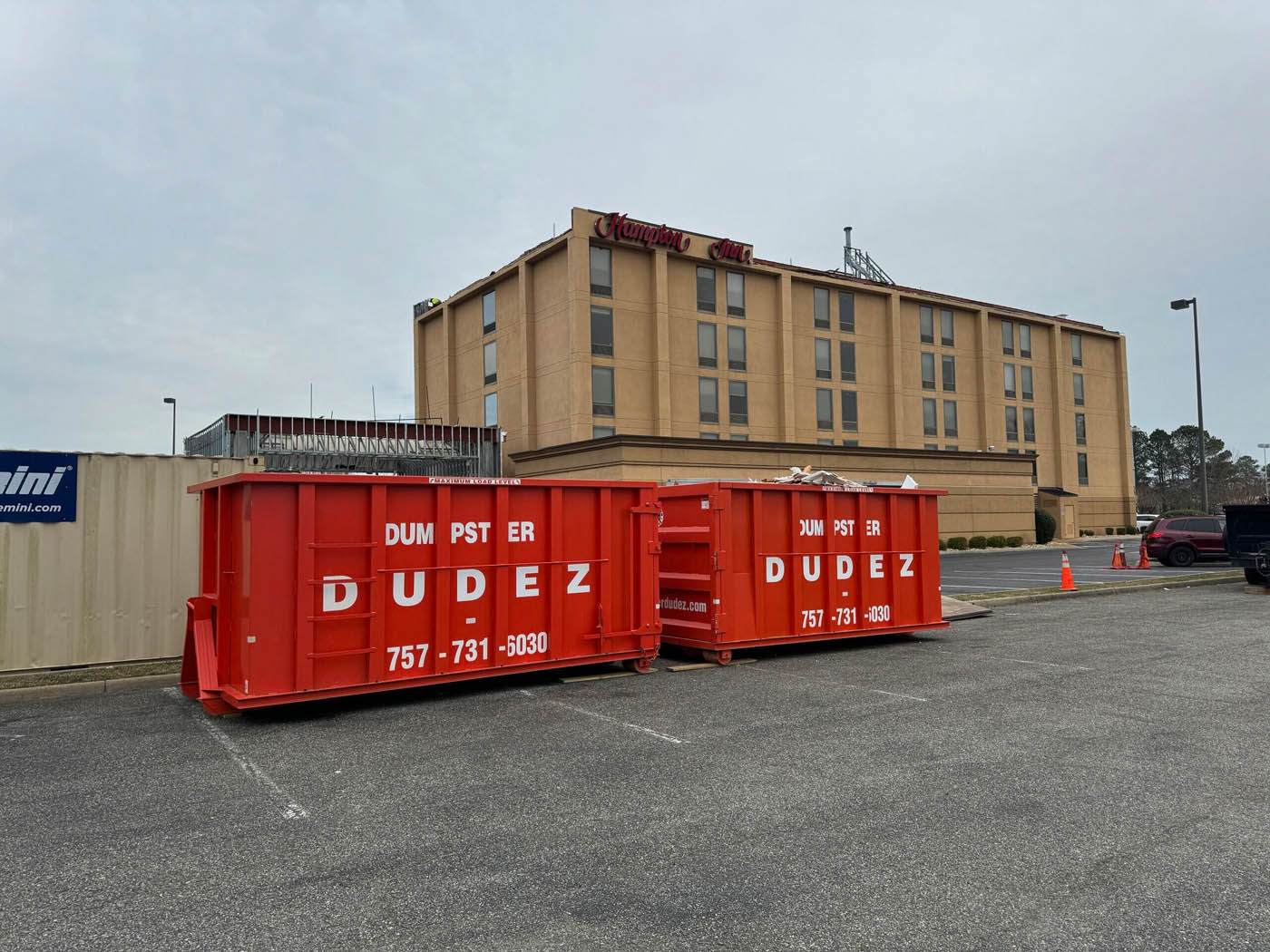 A construction dumpster from Dumpster Dudez in front of a commercial project.