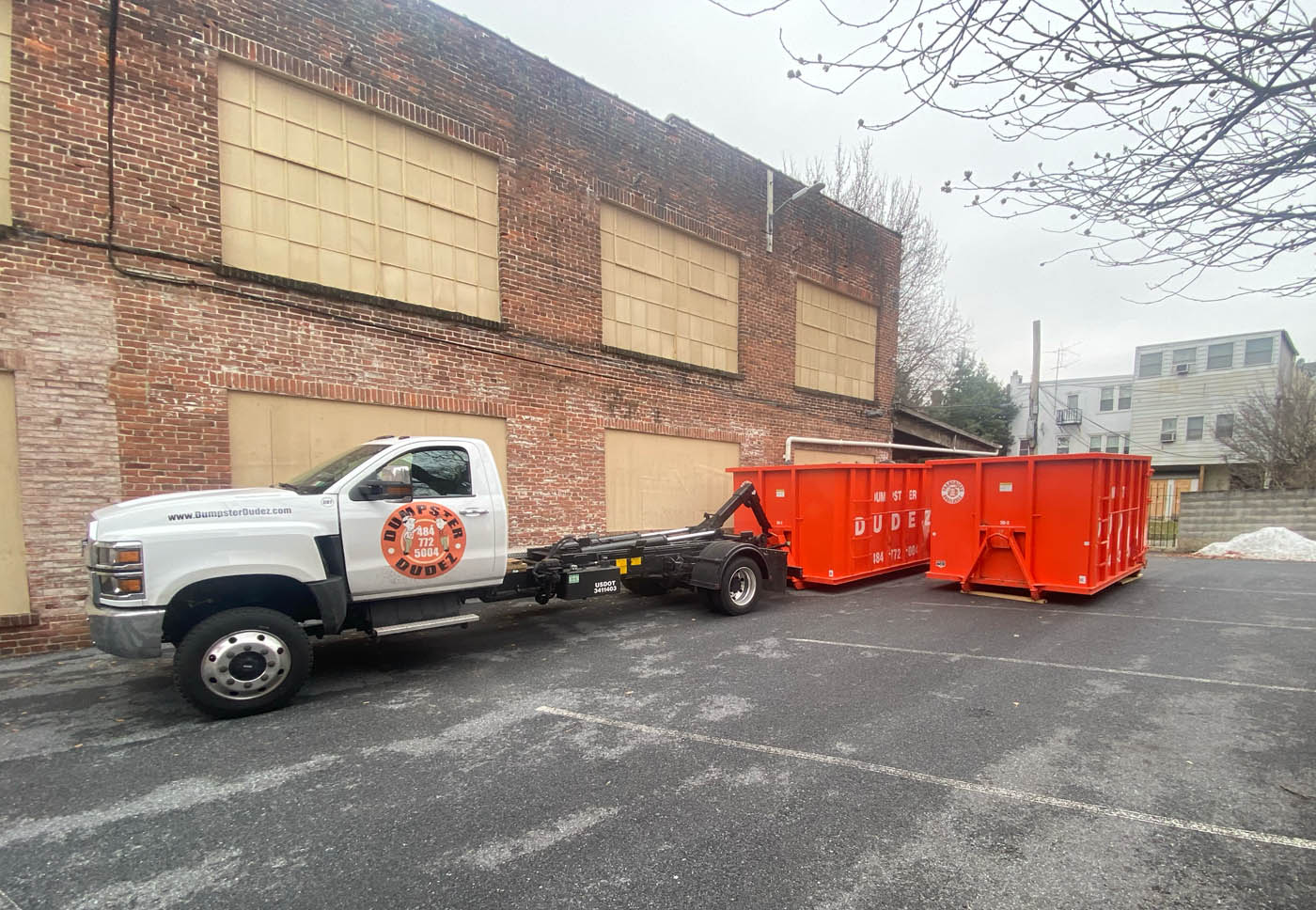 
				A small, white, Rochester 20 yard dumpster rental truck parked behind a commercial building.
			